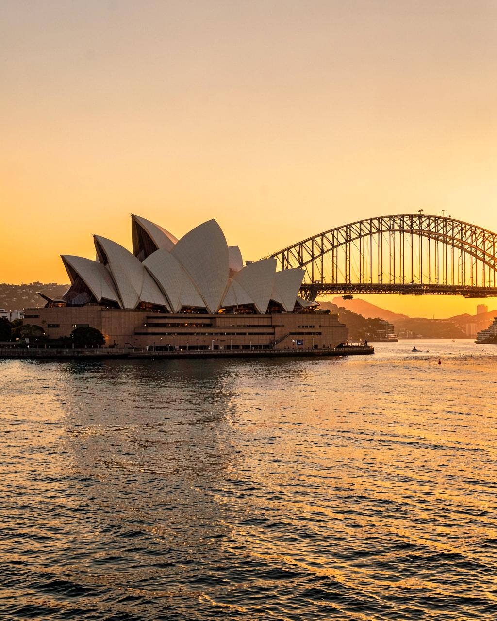 Sydney Opera House and Harbour Bridge at sunset with golden light on the water