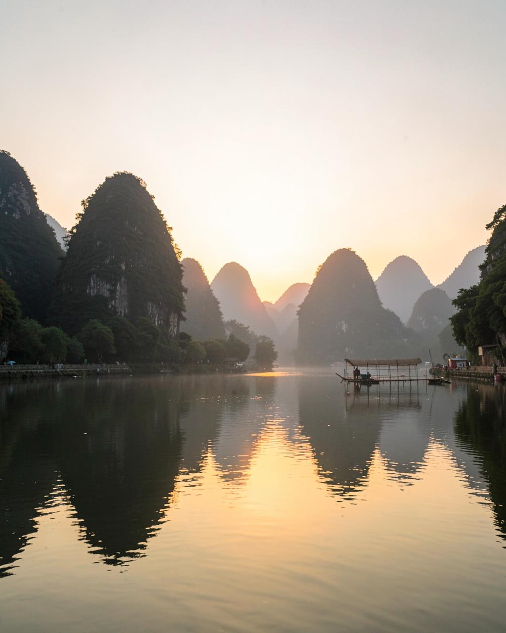 Sunrise over Guilin karst mountains reflected in the Li River with a bamboo raft in the distance
